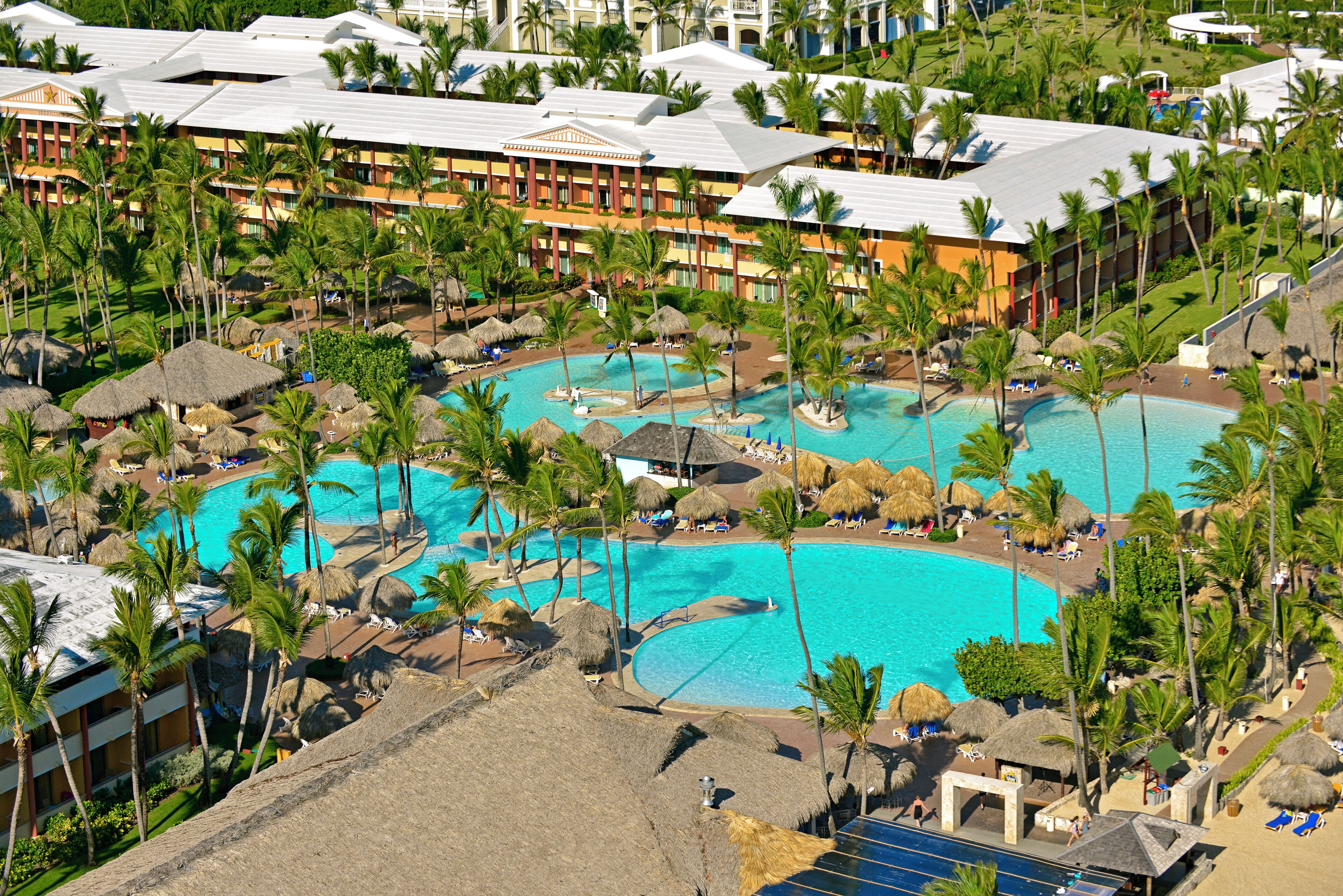 Un resort con varias piscinas rodeado de palmeras y sombrillas de paja.