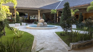 A courtyard with a central water feature, surrounded by greenery and a covered seating area.