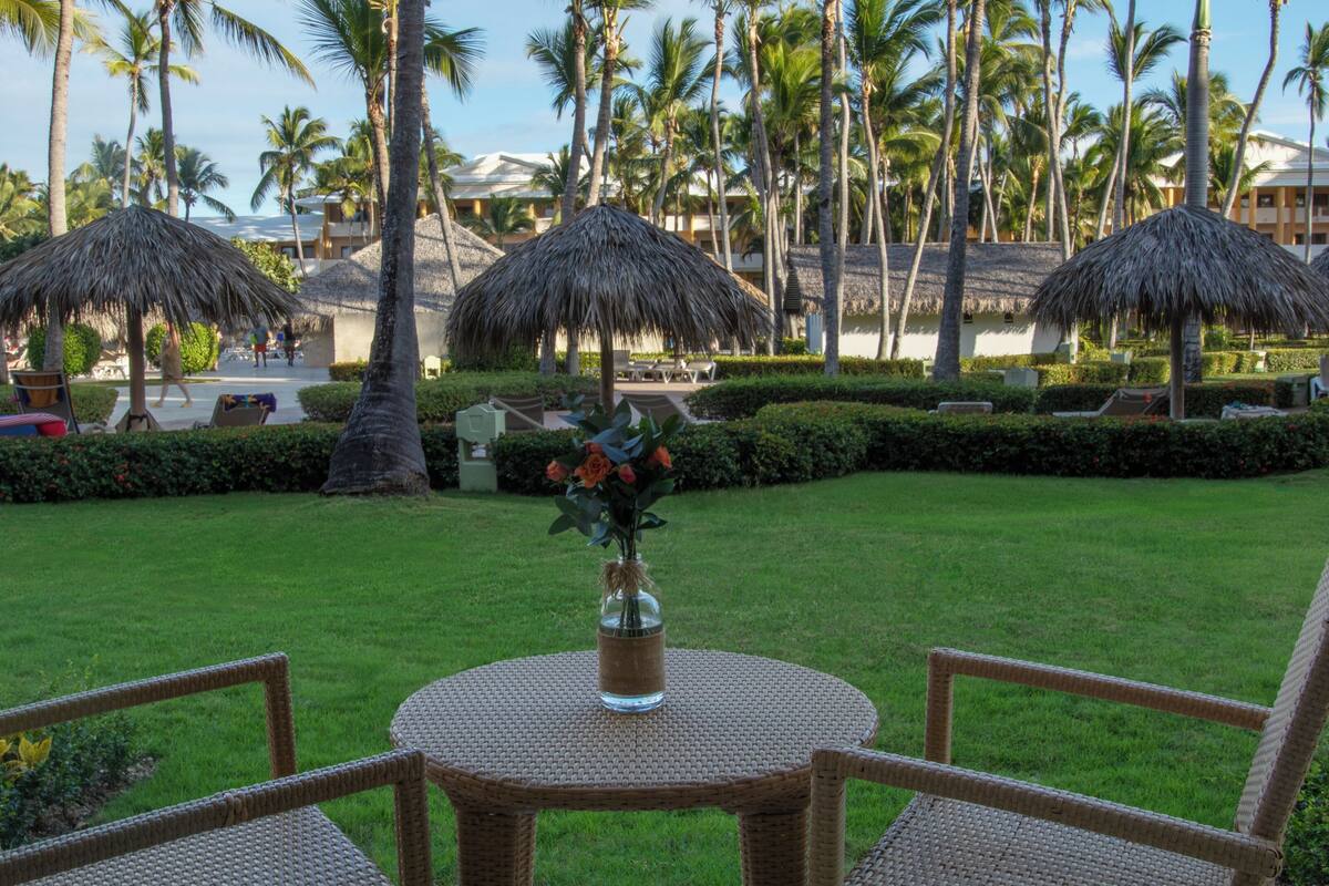 A tropical resort setting with thatched umbrellas, palm trees, and a grassy lawn.