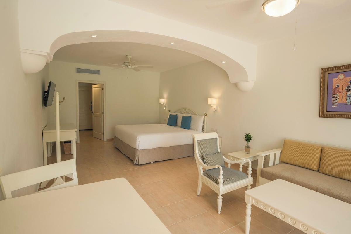 A hotel room with a bed, a chair, a sofa, a small table, and a ceiling fan.
