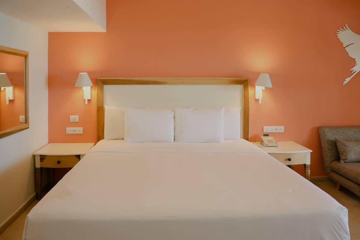 A hotel room with a large bed, two bedside tables, a nightstand, a chair, and a wall-mounted lamp.