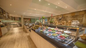 Zona de buffet amb diverses opcions de menjar, un xef preparant plats i una paret decorativa amb plantes i escultures.