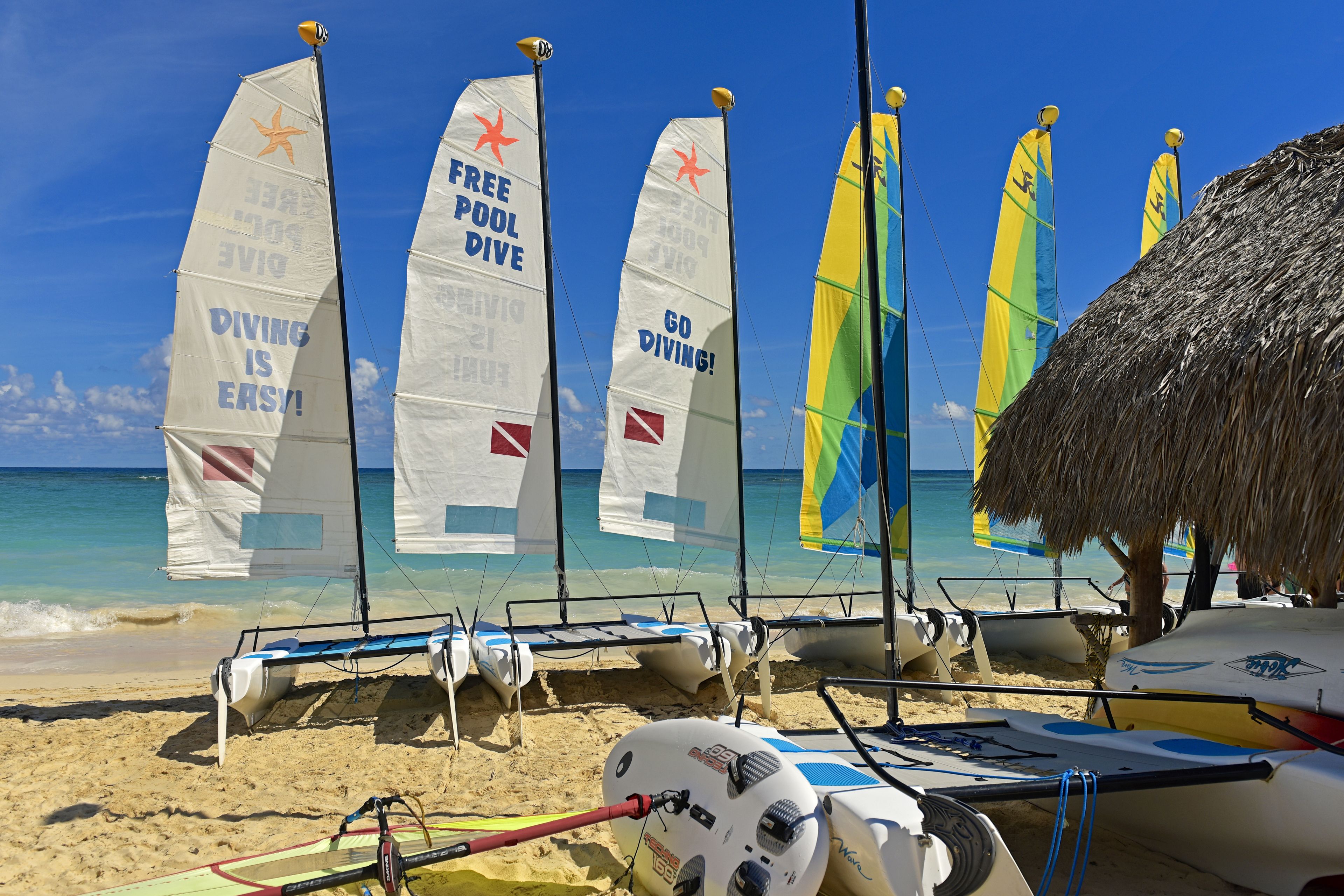 Platja amb diverses taules de vela i un parasol de palla.