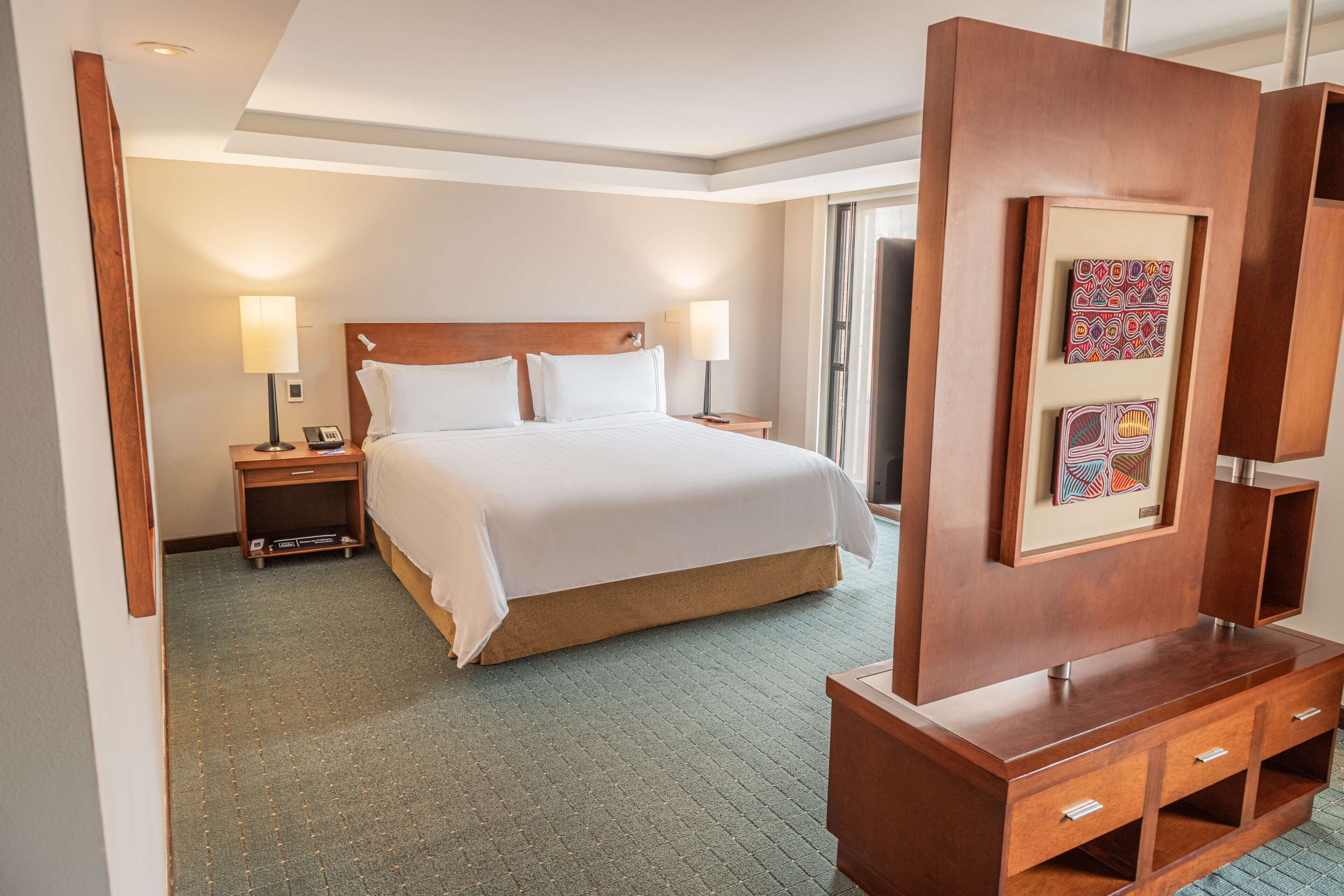 A hotel room with a bed, bedside tables, a dresser, and a large mirror.
