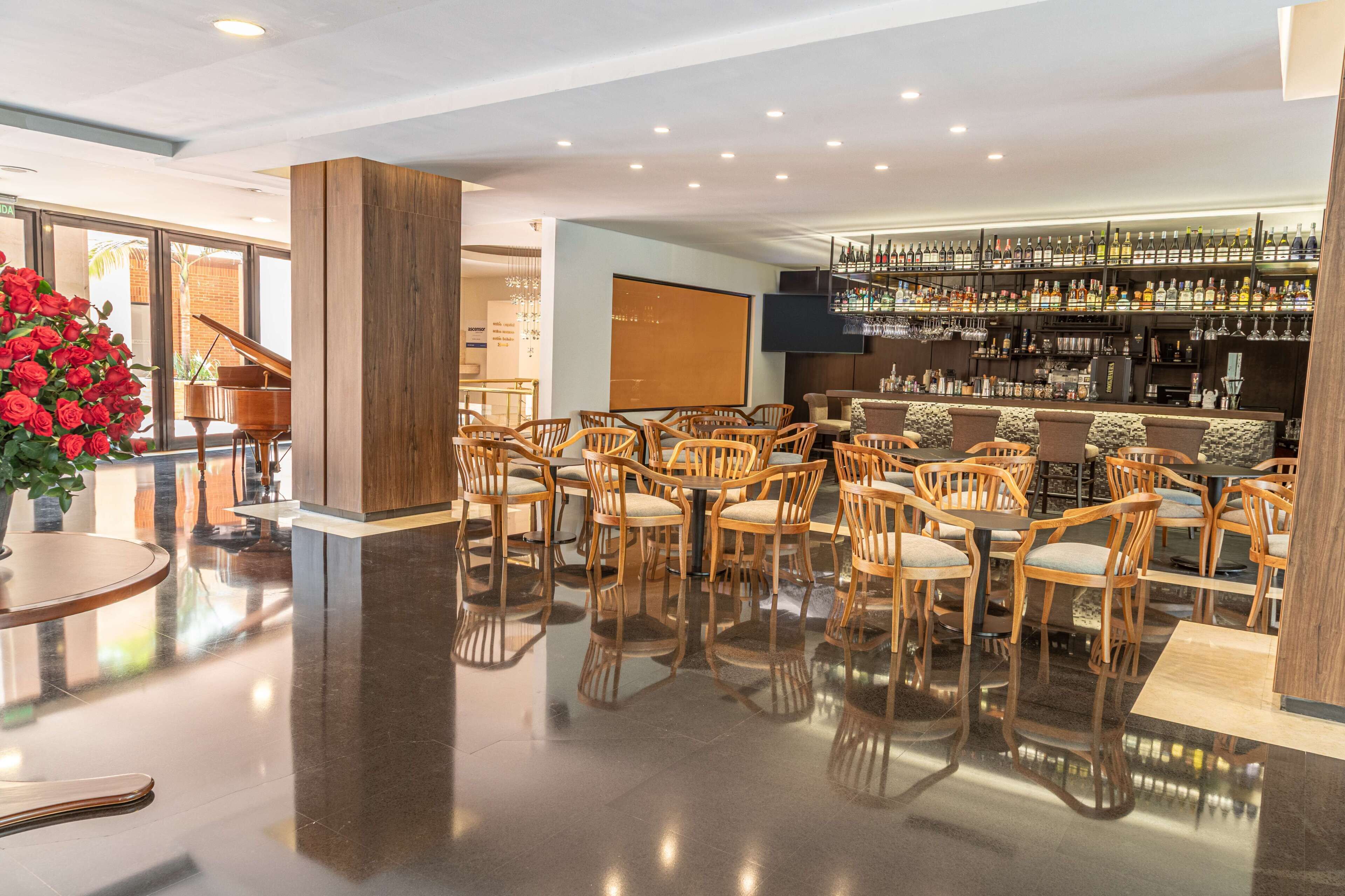 Een hotellobby met een piano, een barruimte met drankenkasten en een zithoek met houten stoelen en tafels.