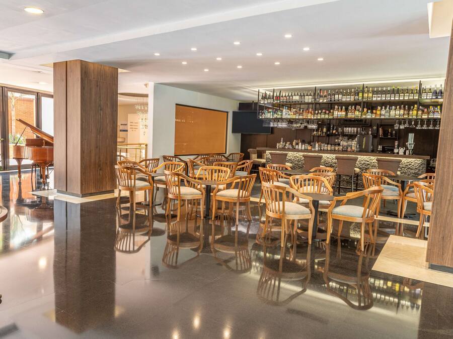 Eine Hotlellobby mit einem Klavier, einer Bar mit Spirituosenregalen und einer Sitzecke mit Holztischen und -stühlen.