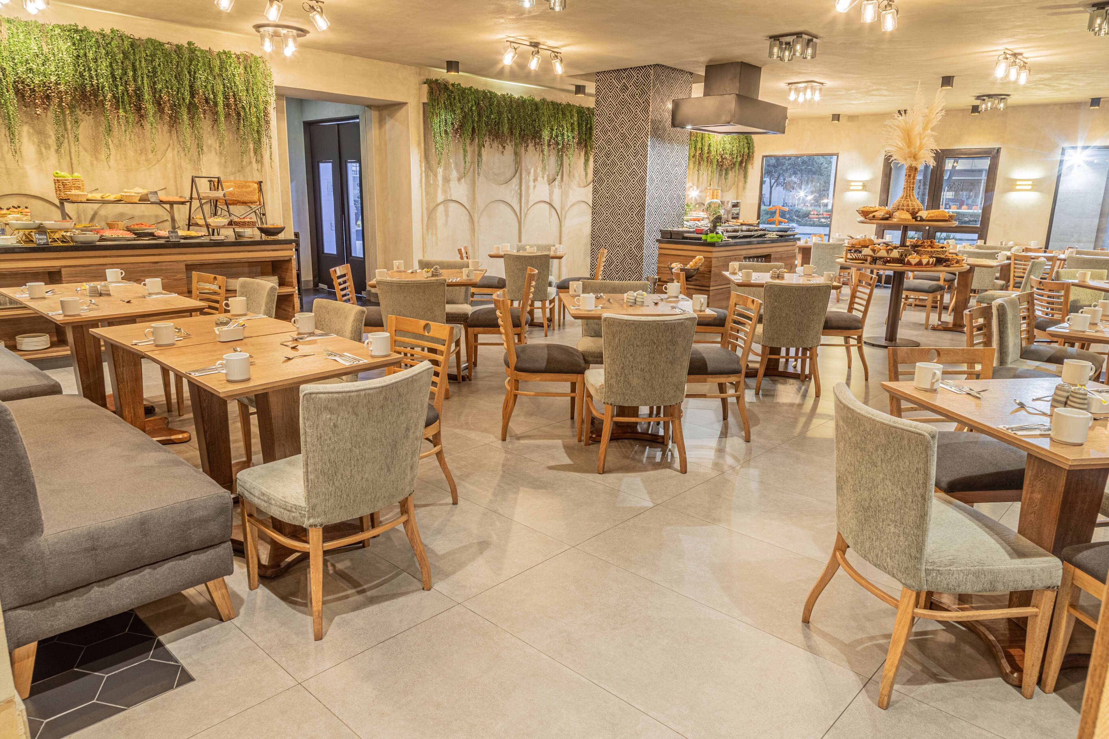 A restaurant with multiple tables and chairs, a buffet area, and a wall decorated with hanging plants.