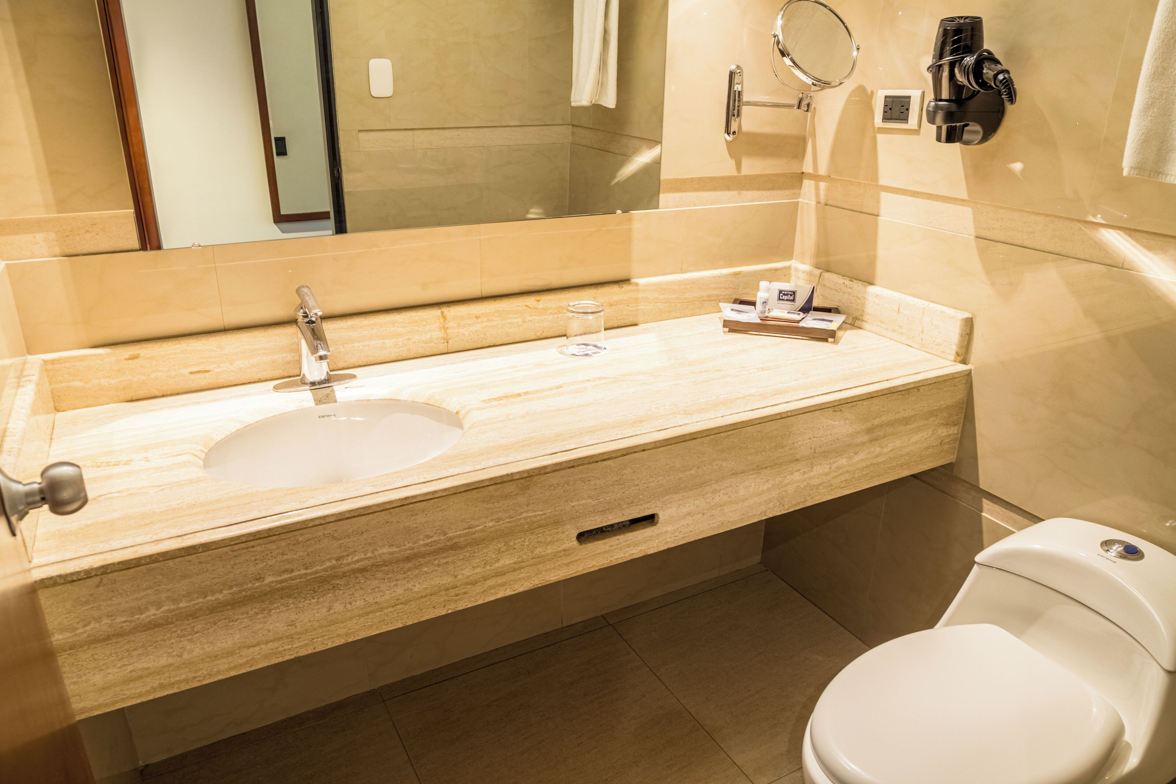 Un baño con tocador color beige, un lavabo, un espejo, un perchero para toallas y un inodoro.