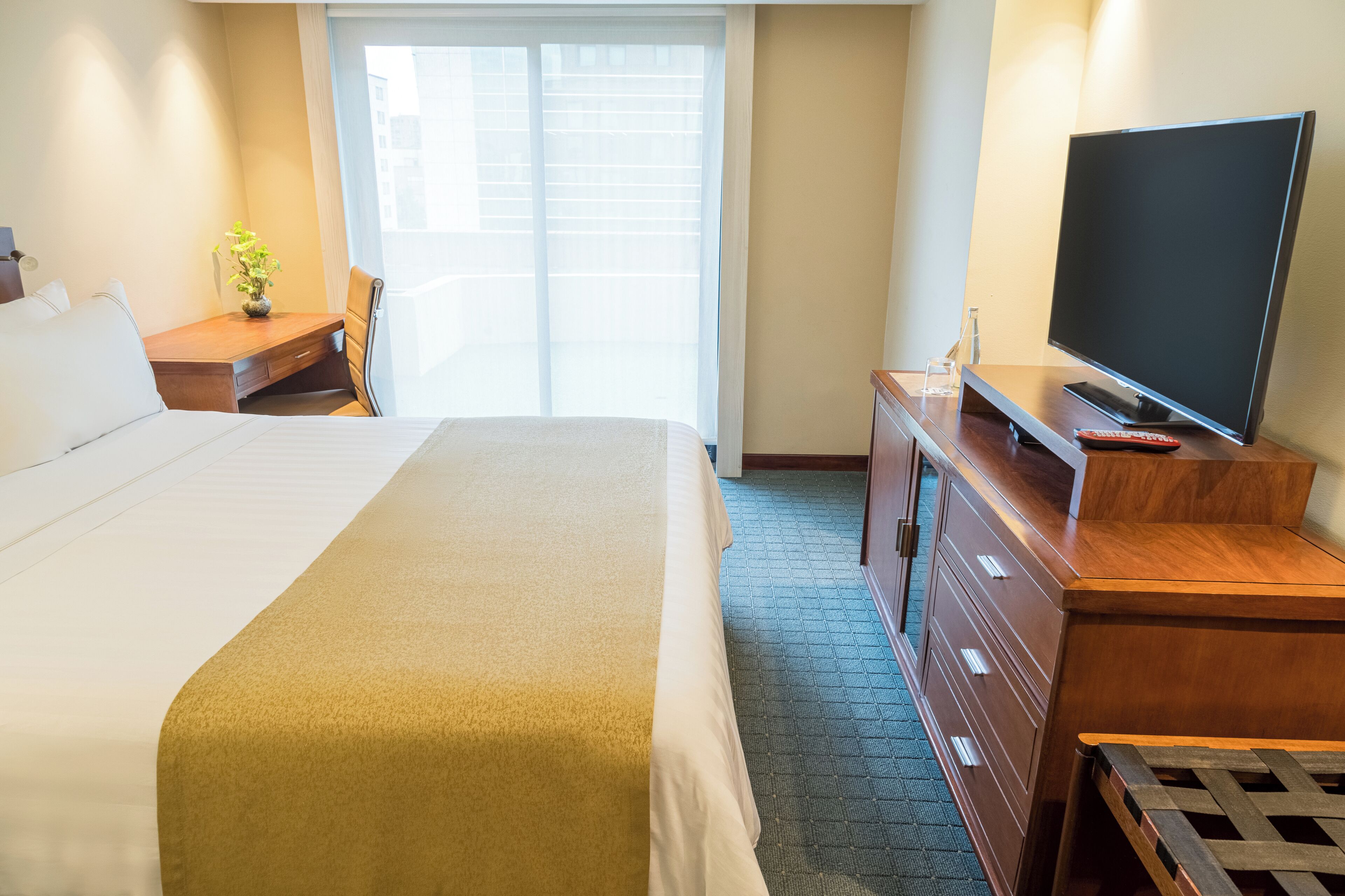 Een hotelkamer met een groot bed, een houten dressoir, een televisie en een tafeltje met een plant.
