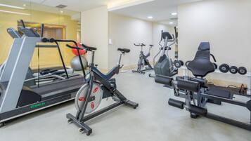 Un gimnasio con máquinas de cardio, mancuernas y un espejo grande.