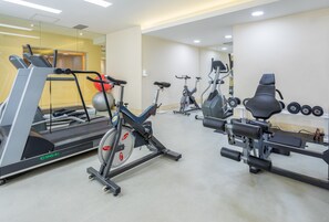A gym with cardio machines, dumbbells, and a mirrored wall.