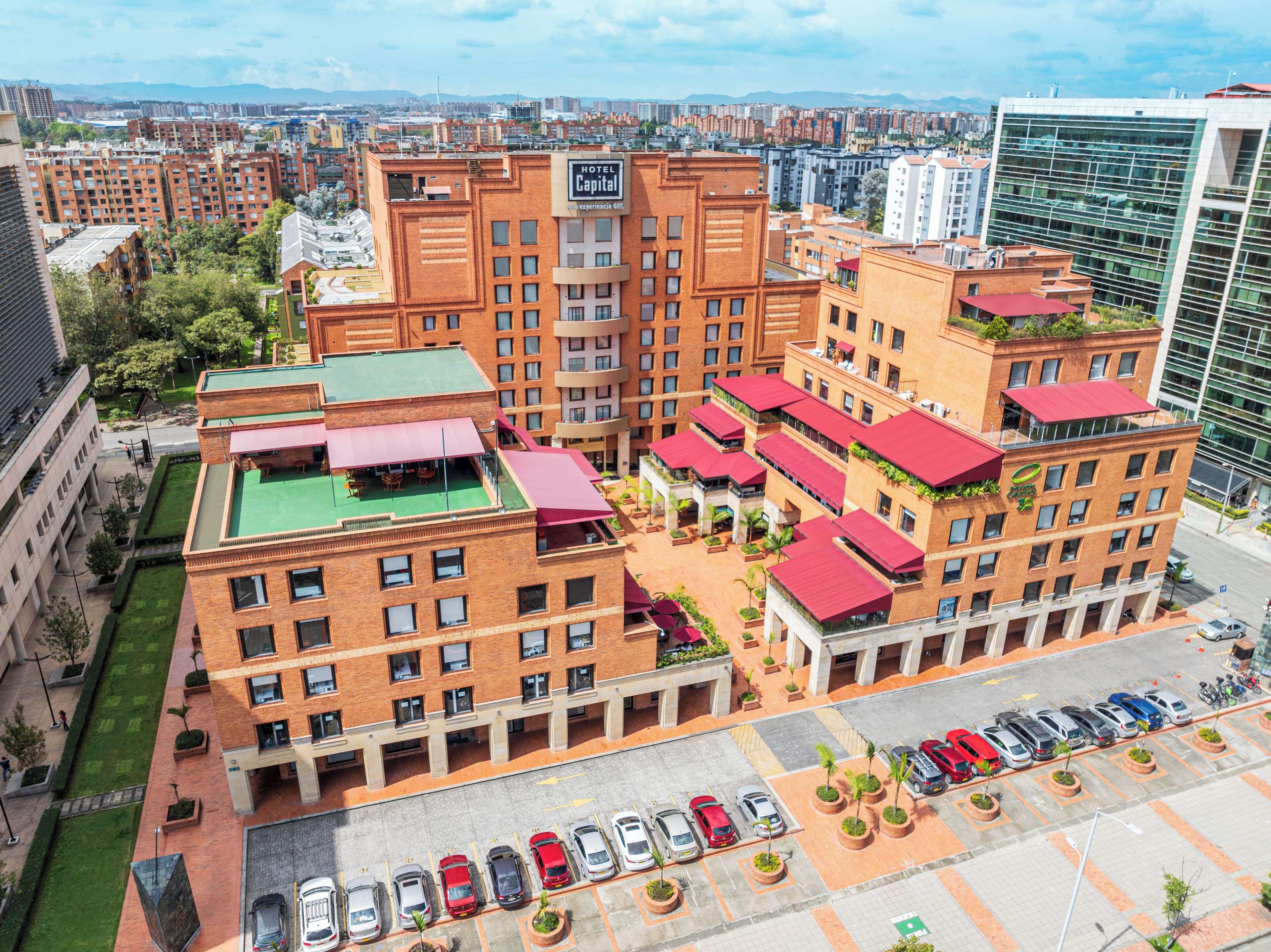 Um hotel com vários andares, terraço no telhado, estacionamento e vista para a paisagem urbana.
