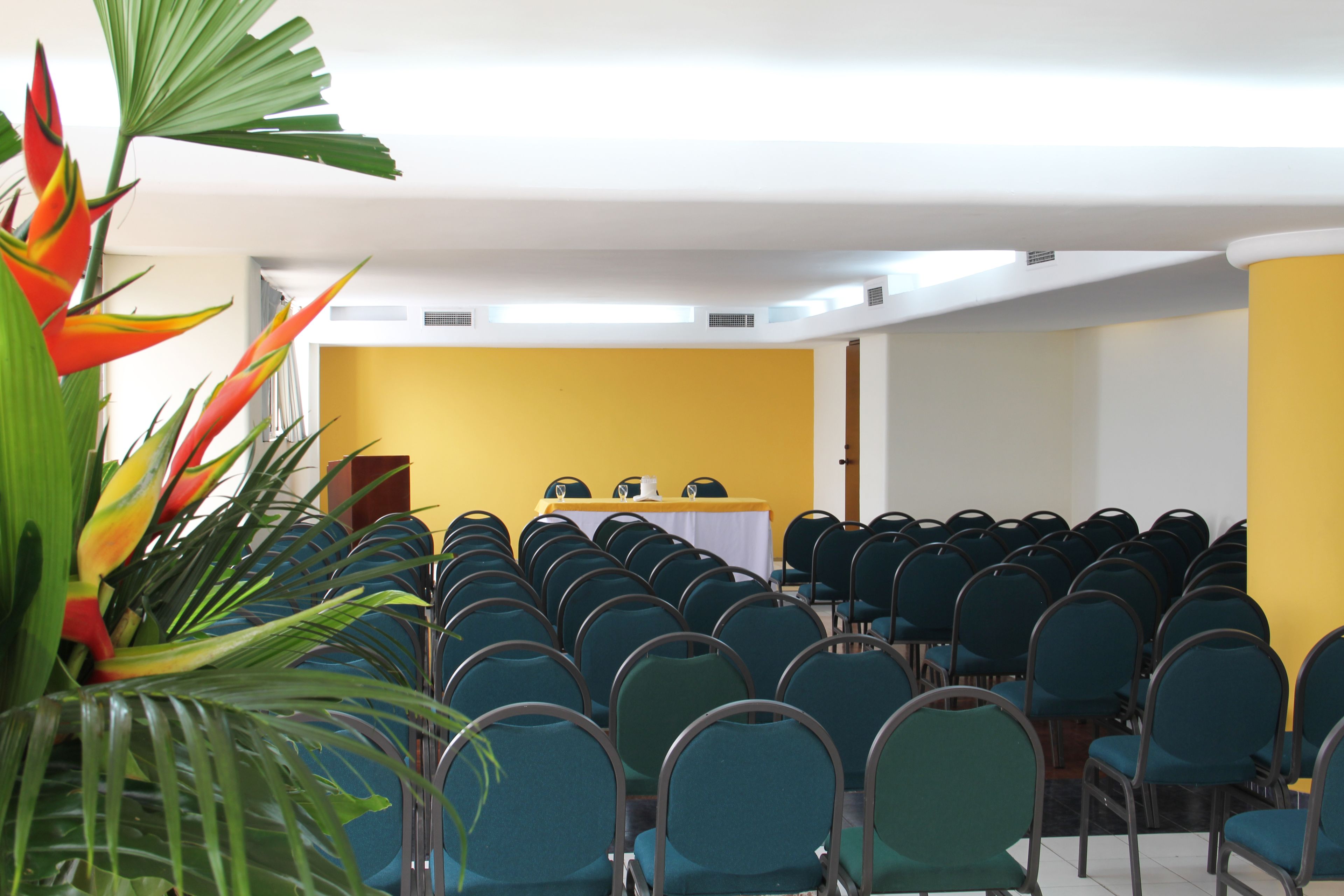 A conference room with rows of chairs, a table with a white tablecloth, and a yellow wall.