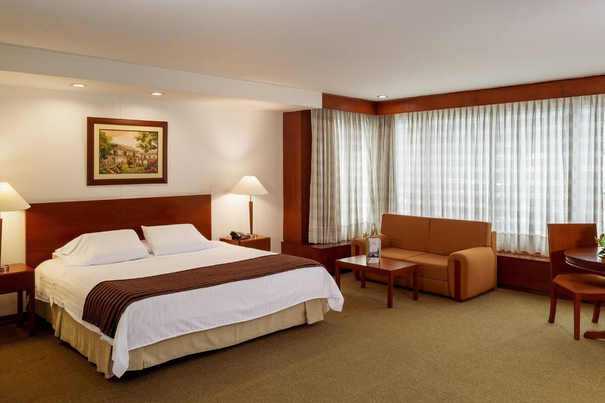 Une chambre d’hôtel avec un grand lit, un canapé, une petite table et une fenêtre avec des rideaux.