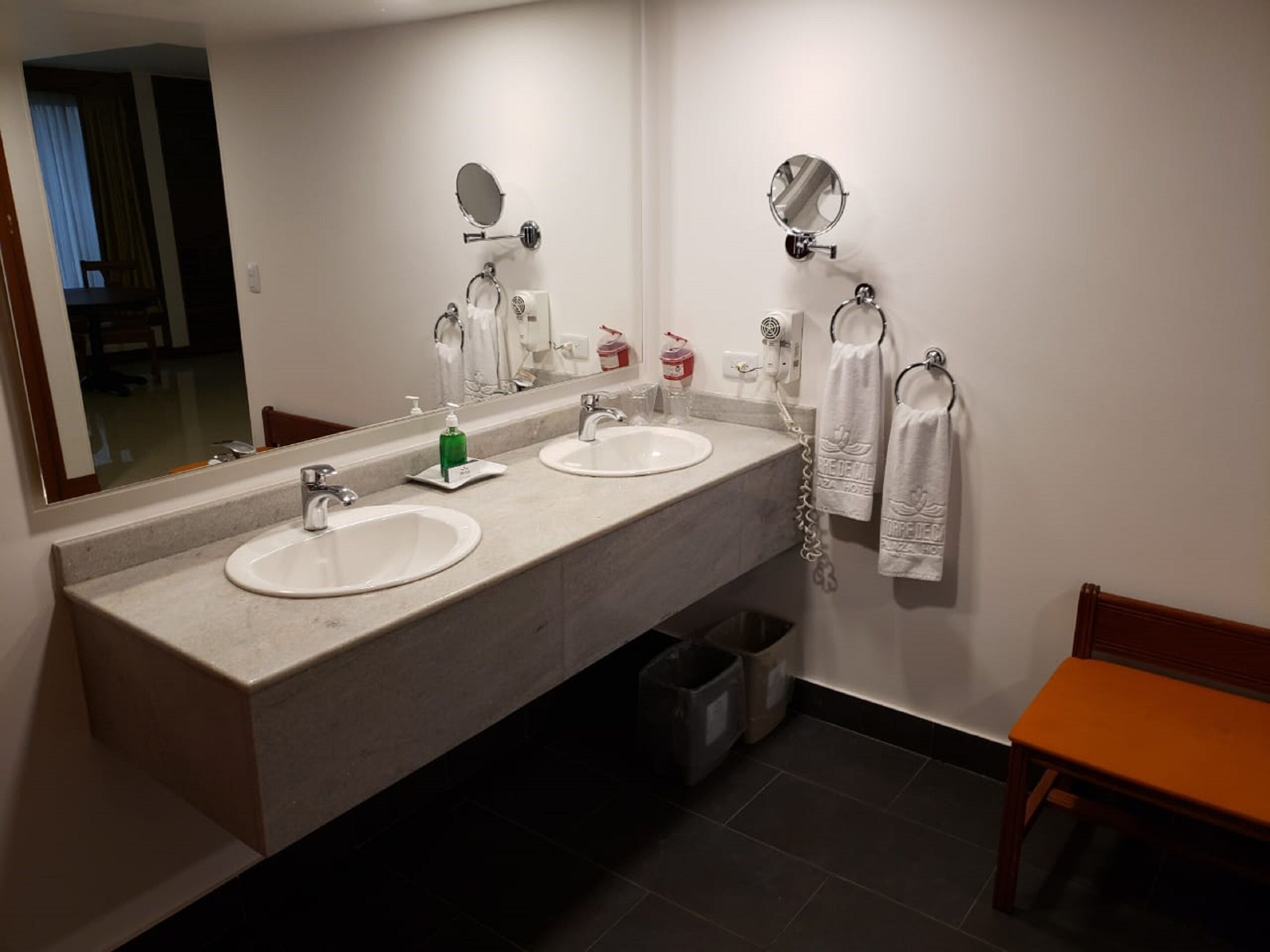 Ein Hotelbad mit zwei Waschbecken, einem großen Spiegel, einem Handtuchhalter und einem Papierkorb.