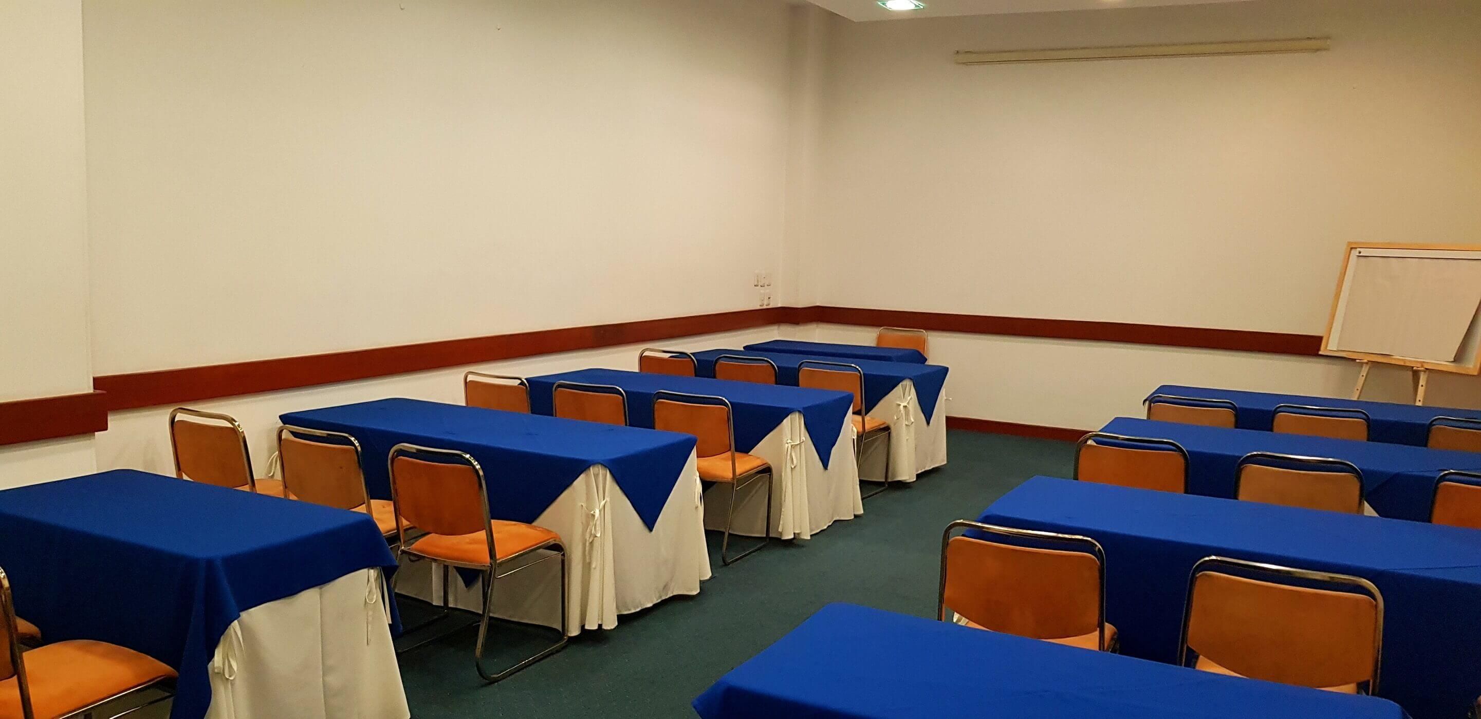 A conference room with tables covered in blue tablecloths and orange chairs.