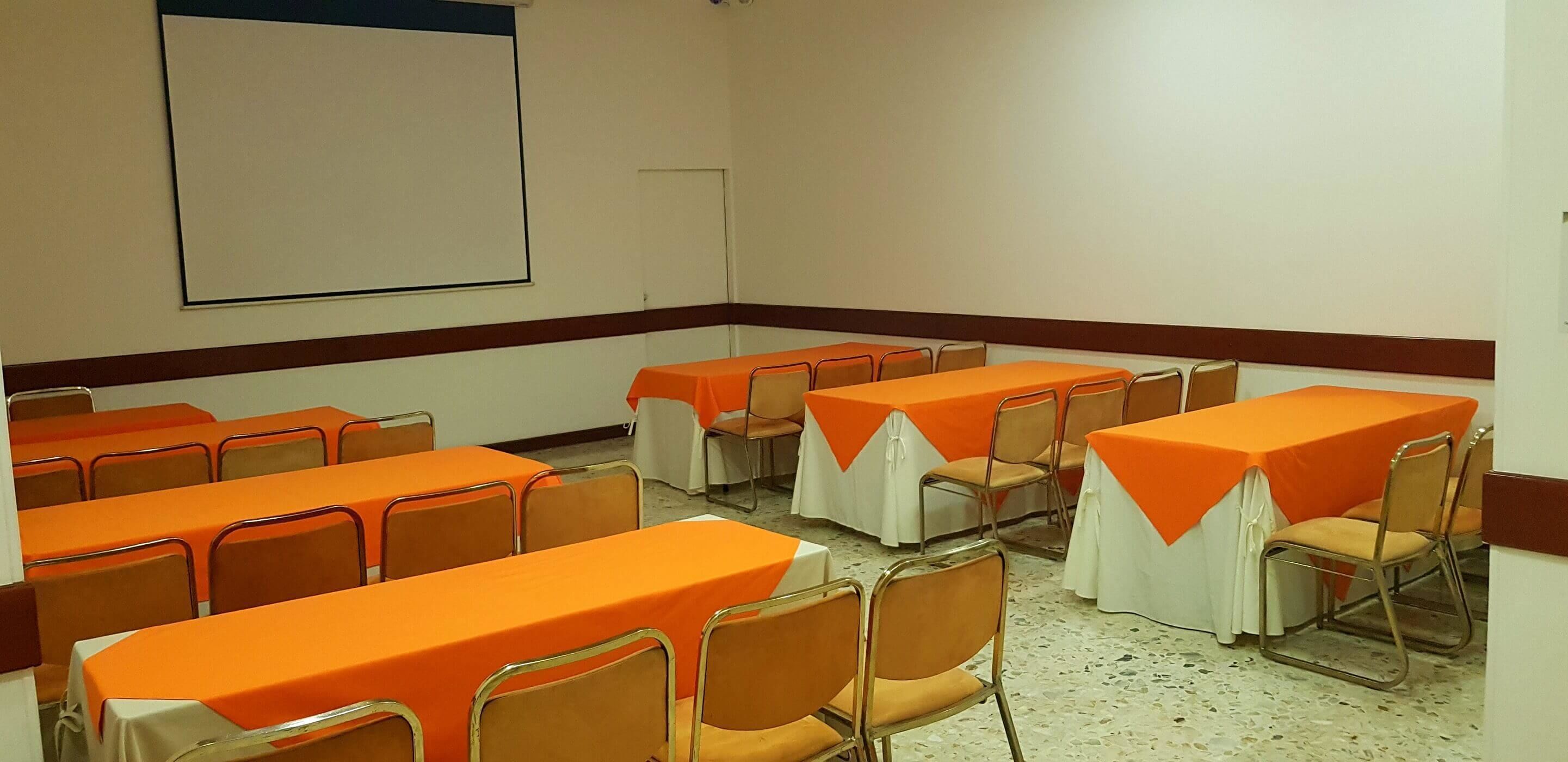 A conference room with multiple tables and chairs, arranged in rows.