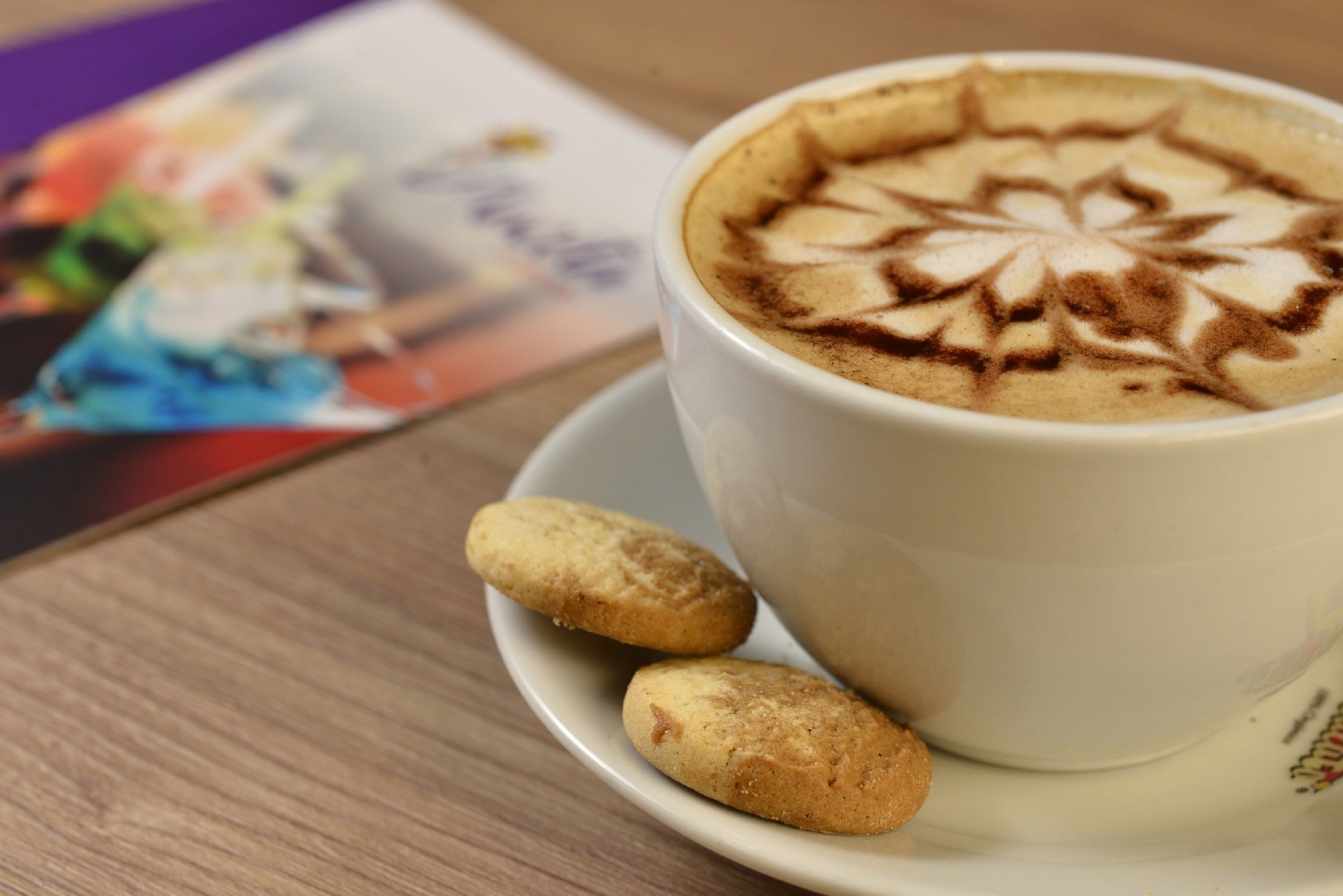 A cup of coffee with latte art on a saucer, accompanied by two cookies.