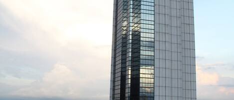 A tall, modern skyscraper with a reflective glass facade, surrounded by other buildings and a clear sky.