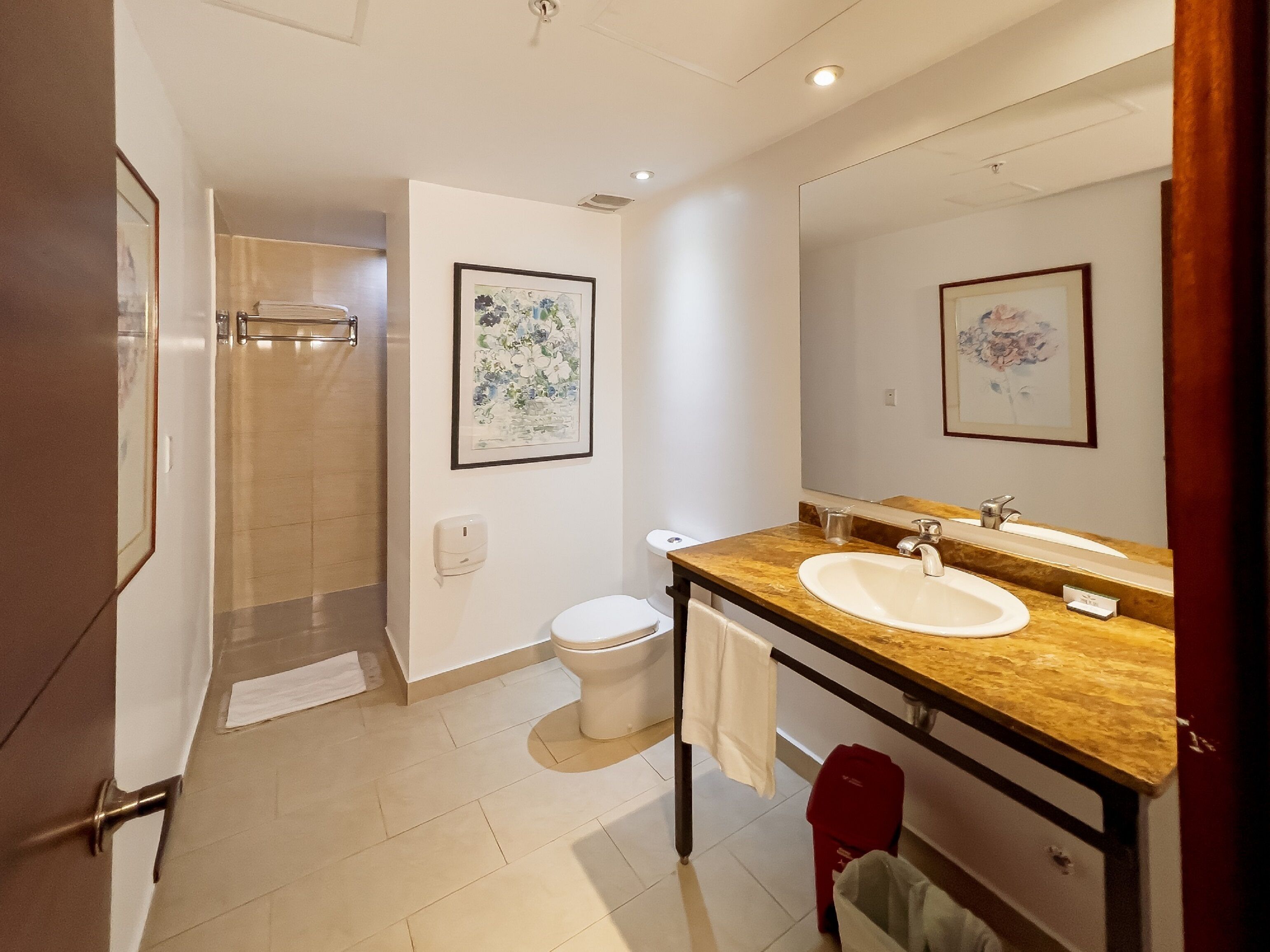 Ein modernes Badezimmer mit Dusche, Toilette und Waschbecken. An den Wänden hängen Bilder in Rahmen und über dem Waschbecken hängt ein großer Spiegel.