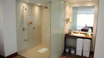 Un baño moderno con ducha envuelta en vidrio, tocador con espejo y ventana que deja entrar luz natural.