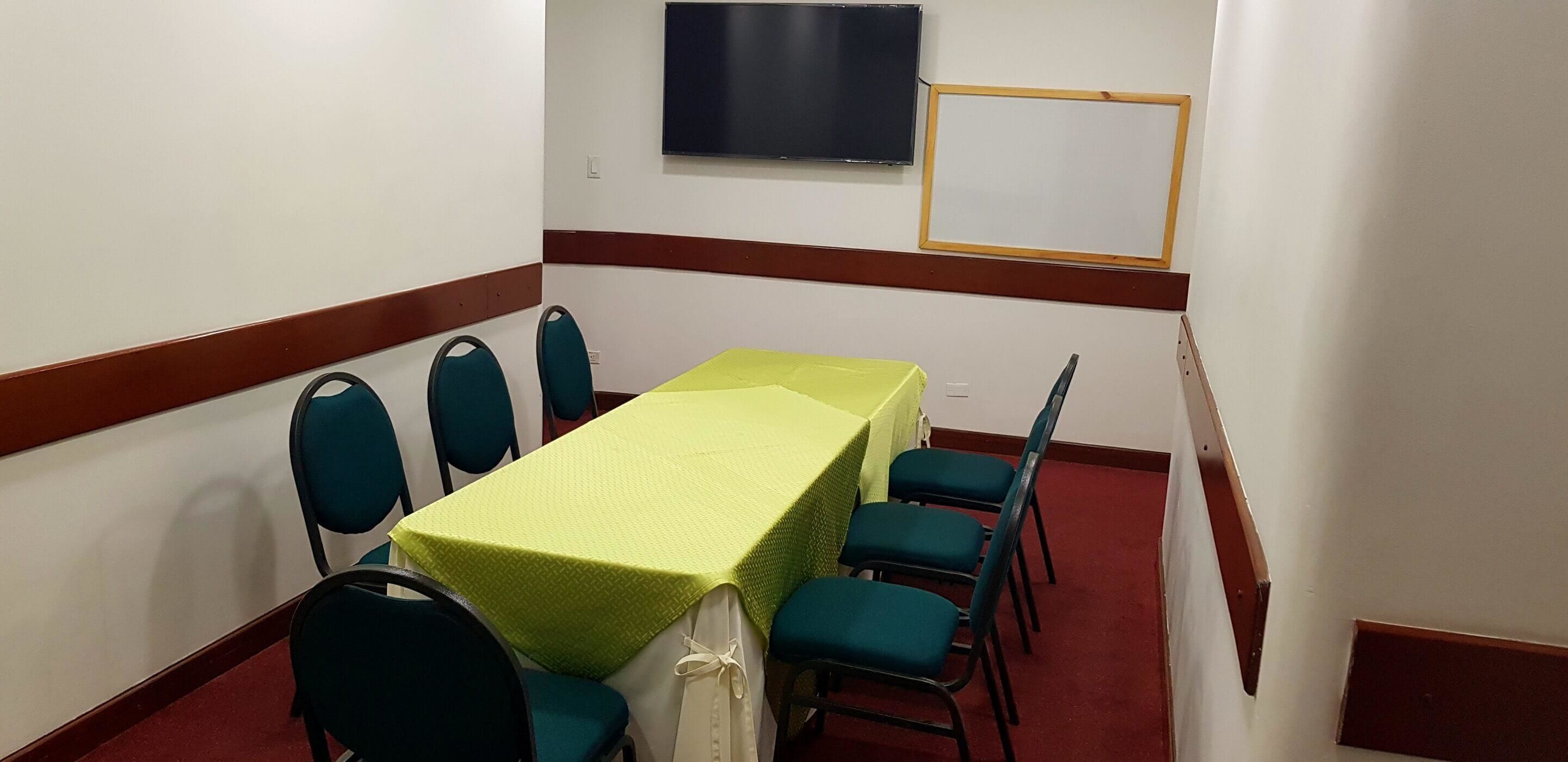 A conference room with a long table, six chairs, a TV, and a whiteboard.