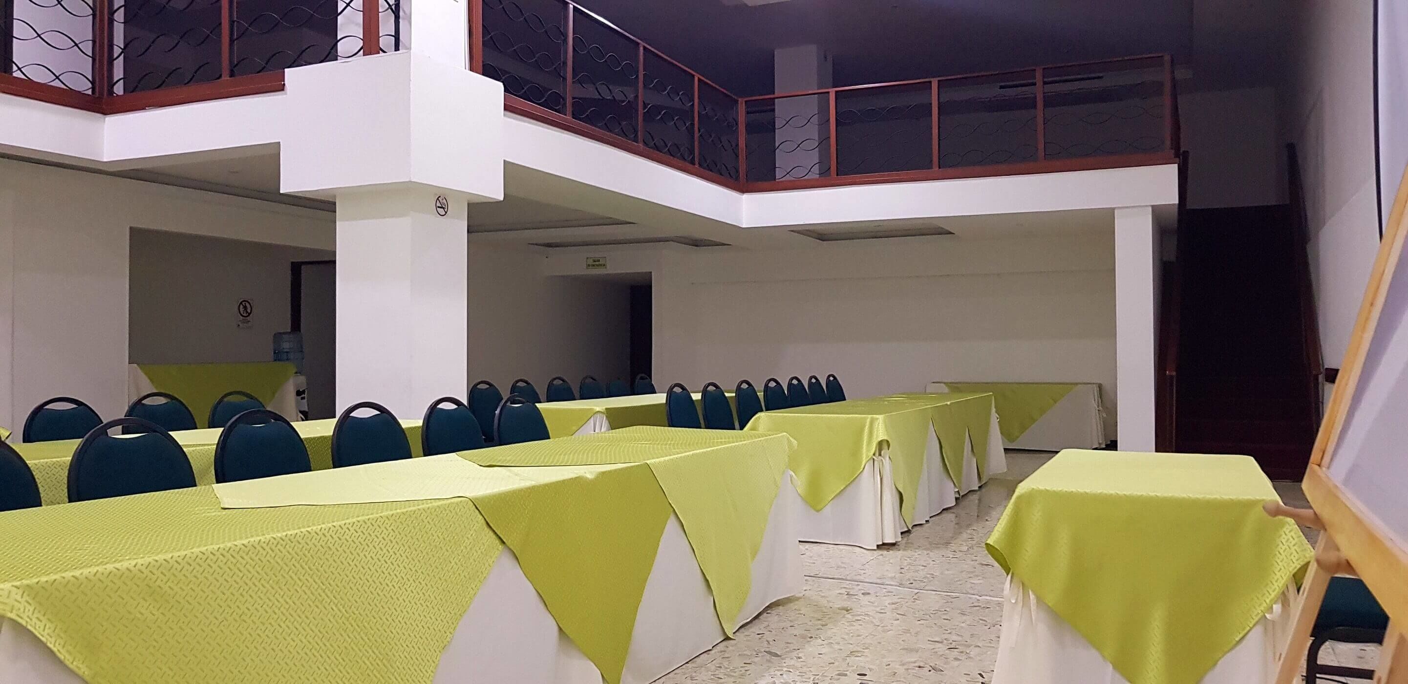 A conference room with multiple tables covered in yellow tablecloths, arranged in rows.