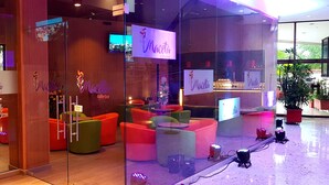 Interior de un café-bar con asientos de colores y una pared de vidrio.