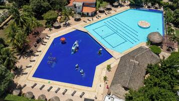 An aerial view of a resort with two swimming pools, a beach area, and a building with a red roof.