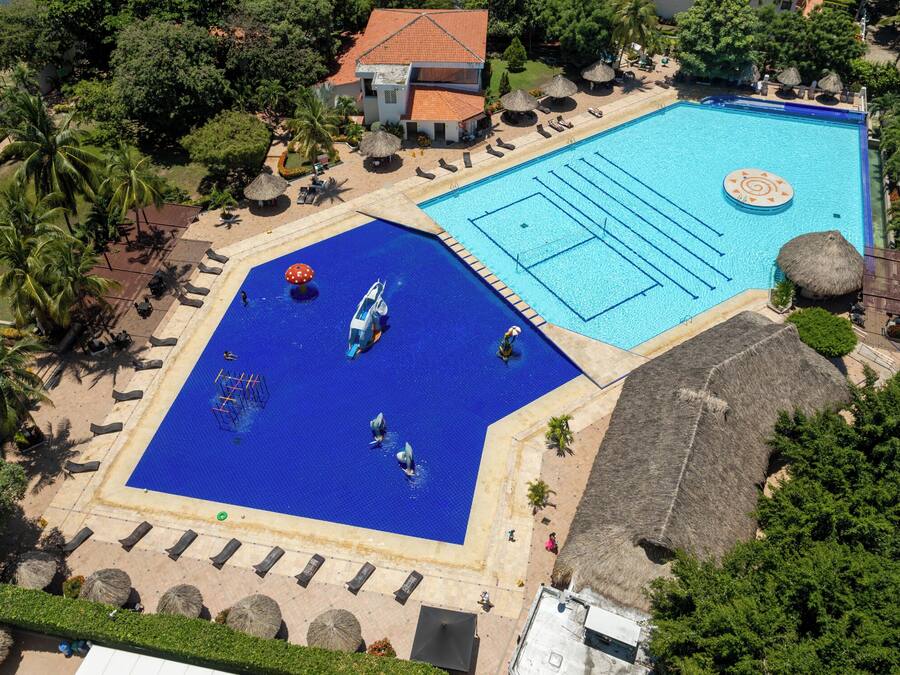 An aerial view of a resort with two swimming pools, a beach area, and a building with a red roof.