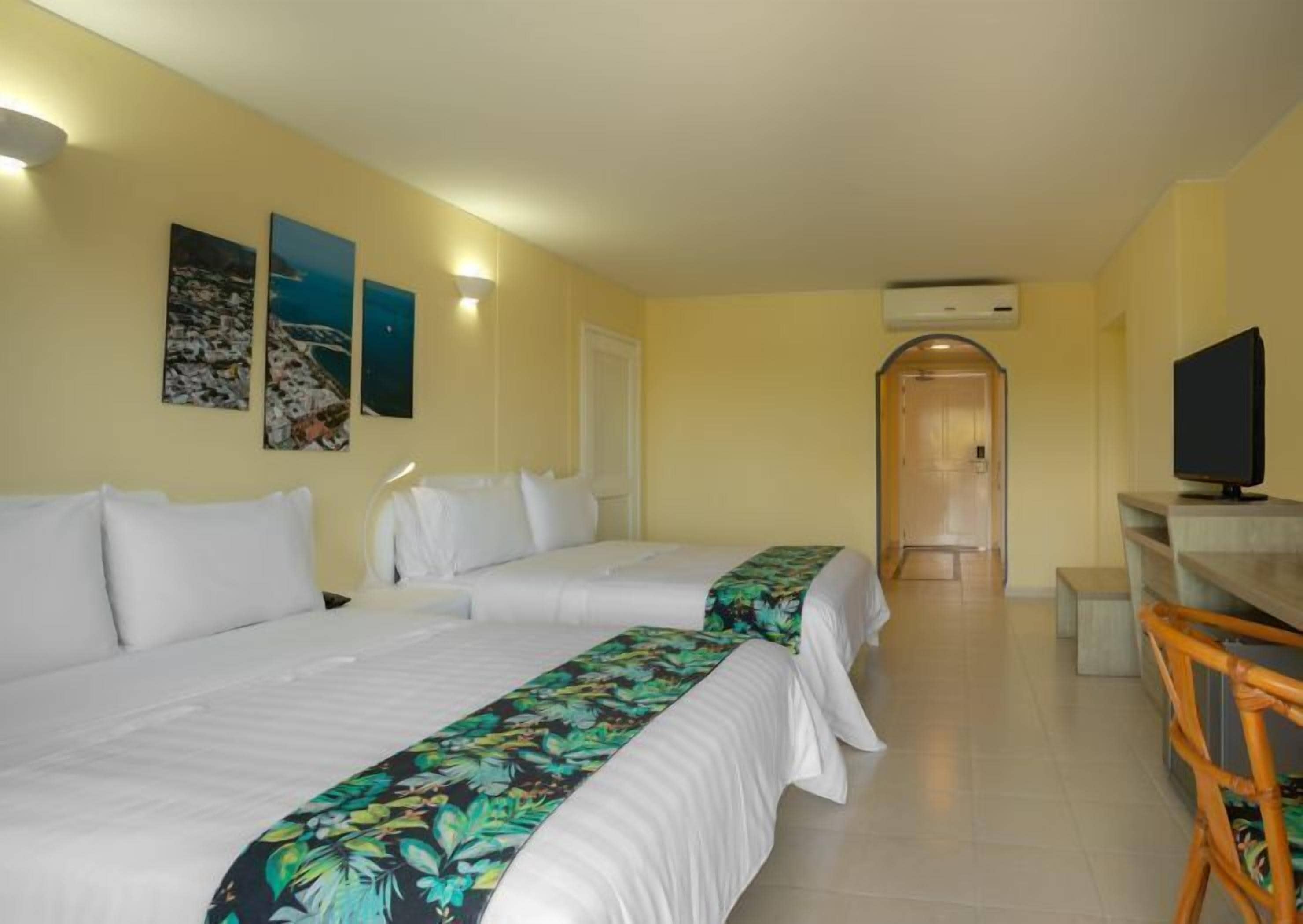A hotel room with two beds, a television, and artwork on the walls.