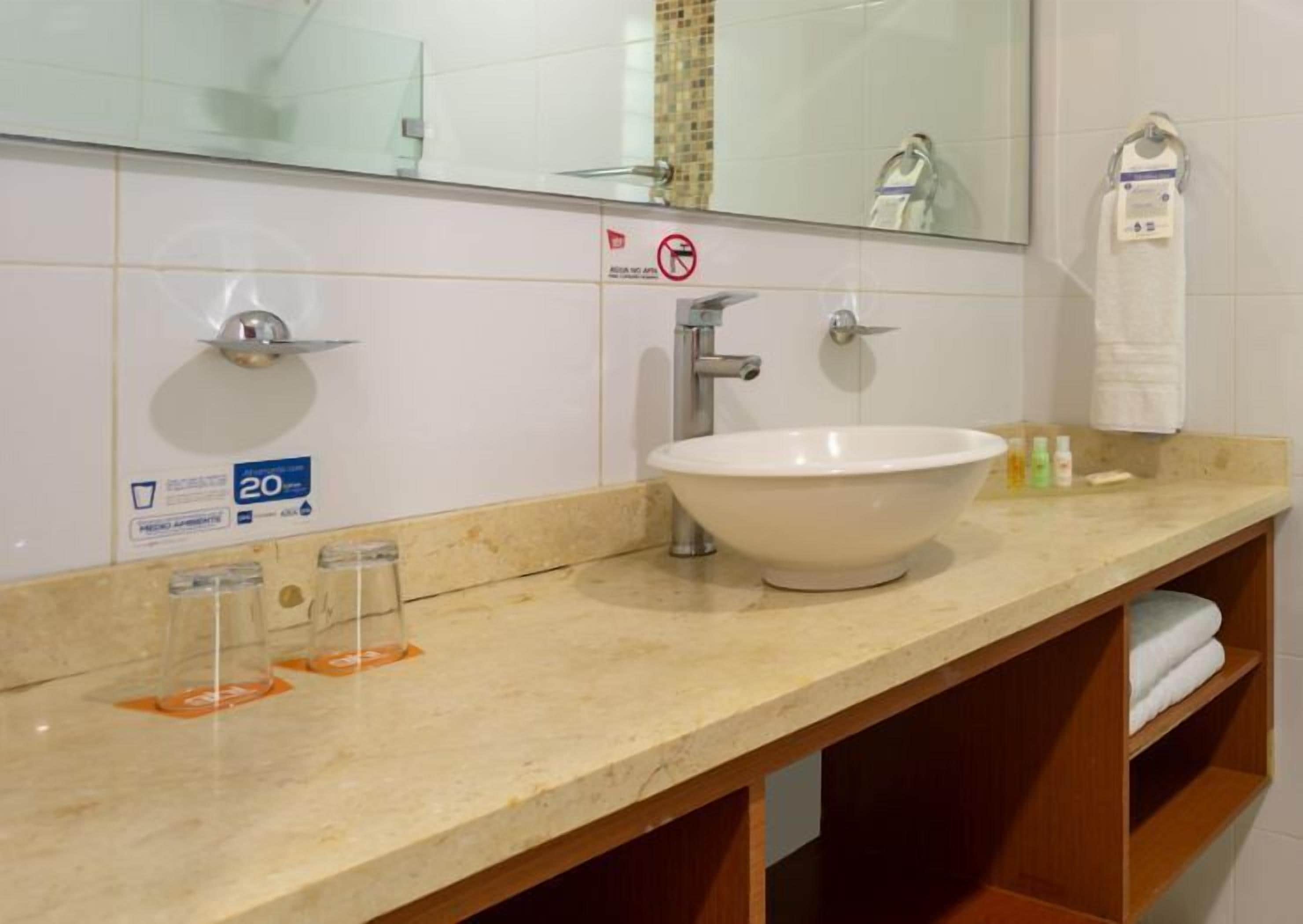 A bathroom with a white sink, a mirror, and a towel rack. There is a sign indicating a 20% discount.