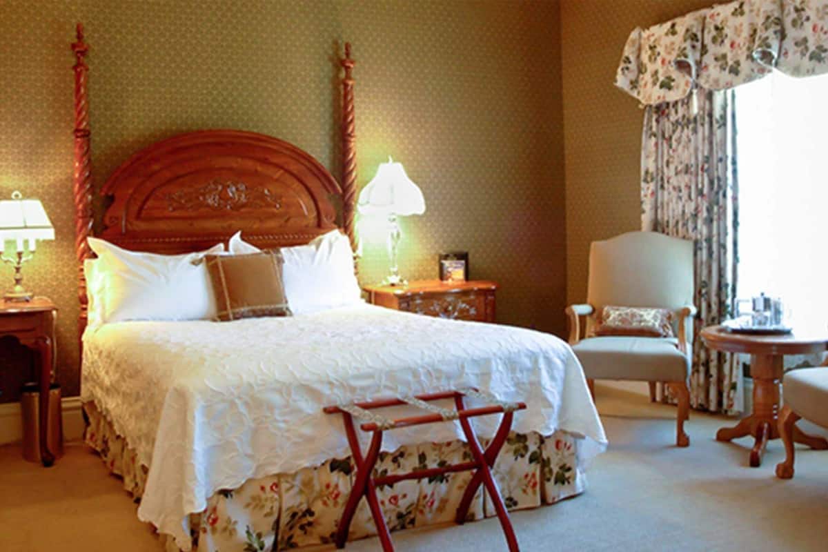 A hotel room with a large bed, a chair, a small table, and a nightstand.