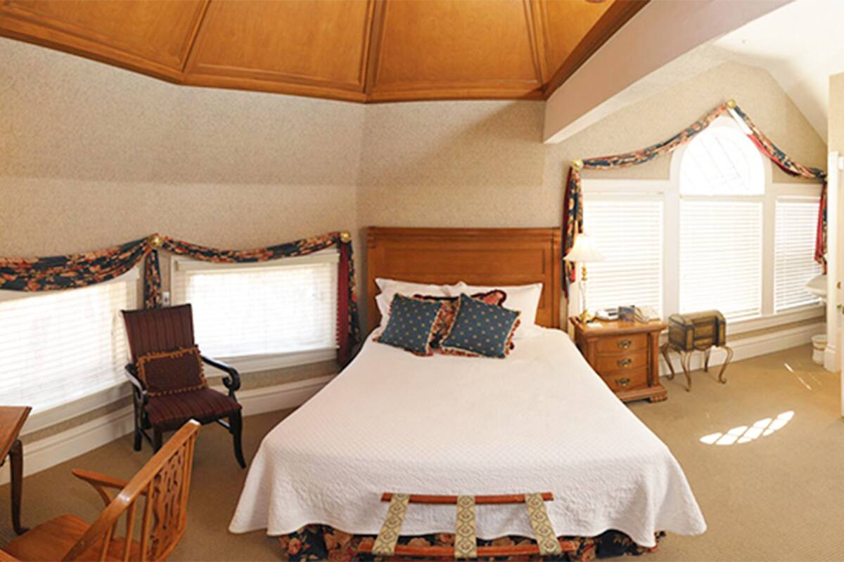 A bedroom with a large bed, a chair, a nightstand, and a window with curtains.