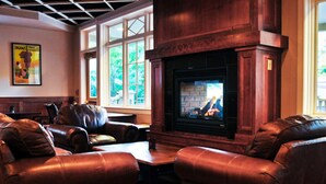 A cozy lounge area with leather sofas, a fireplace, and large windows offering a view of greenery. - Cliff House at Pikes Peak (Manitou Springs)