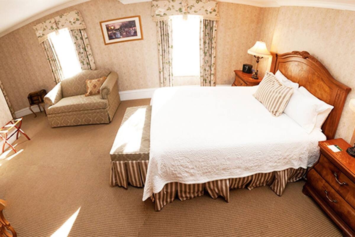 A hotel room with a large bed, a chair, a nightstand, and a window with curtains.