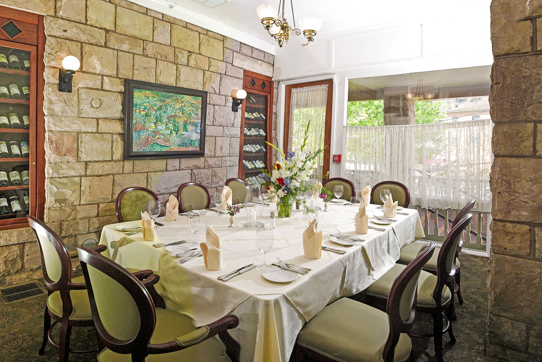 A dining room with a stone wall, a large painting, and a view of greenery outside.