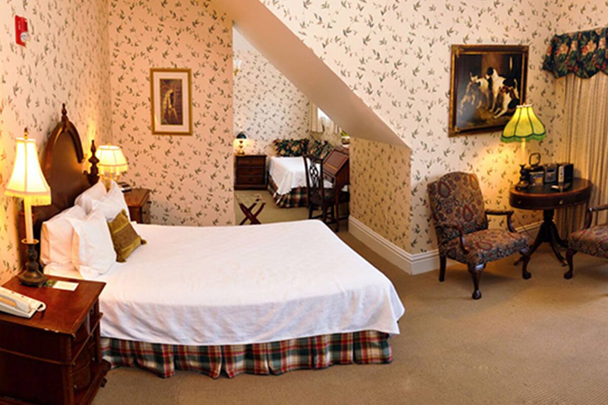 A hotel room with a large bed, a chair, a desk, and a lamp.