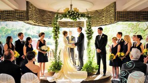 A wedding ceremony with guests seated and standing around a circular stage, decorated with greenery and flowers. - Cliff House at Pikes Peak (Manitou Springs)