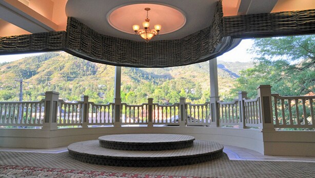 A circular room with a central chandelier, a patterned floor, and a view of a mountainous landscape through large windows. - Cliff House at Pikes Peak (Manitou Springs)