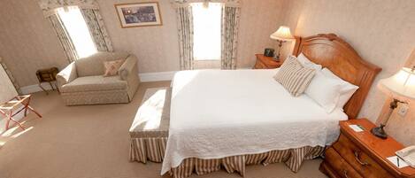 A spacious bedroom with a large bed, a sofa, and a wooden nightstand.
