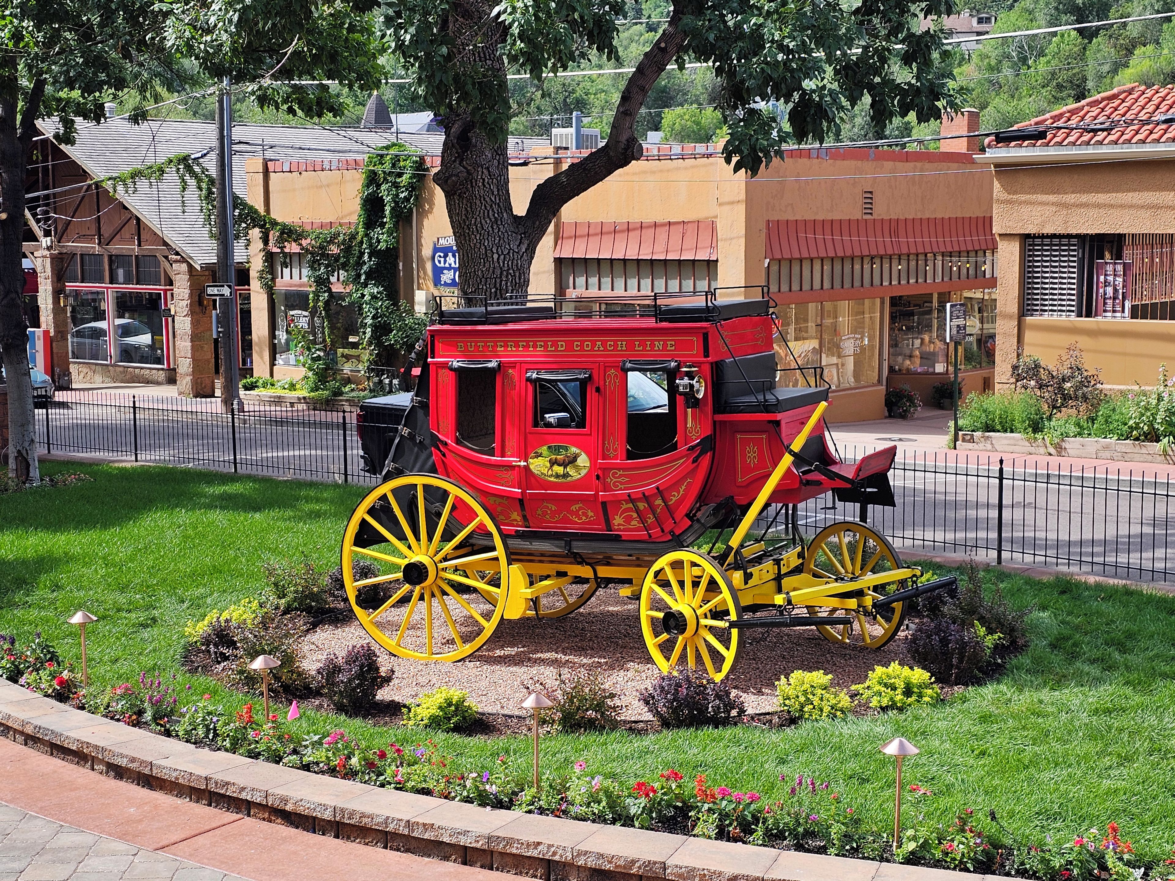 A red and yellow carriage parked in a landscaped area with a tree and a building in the background.