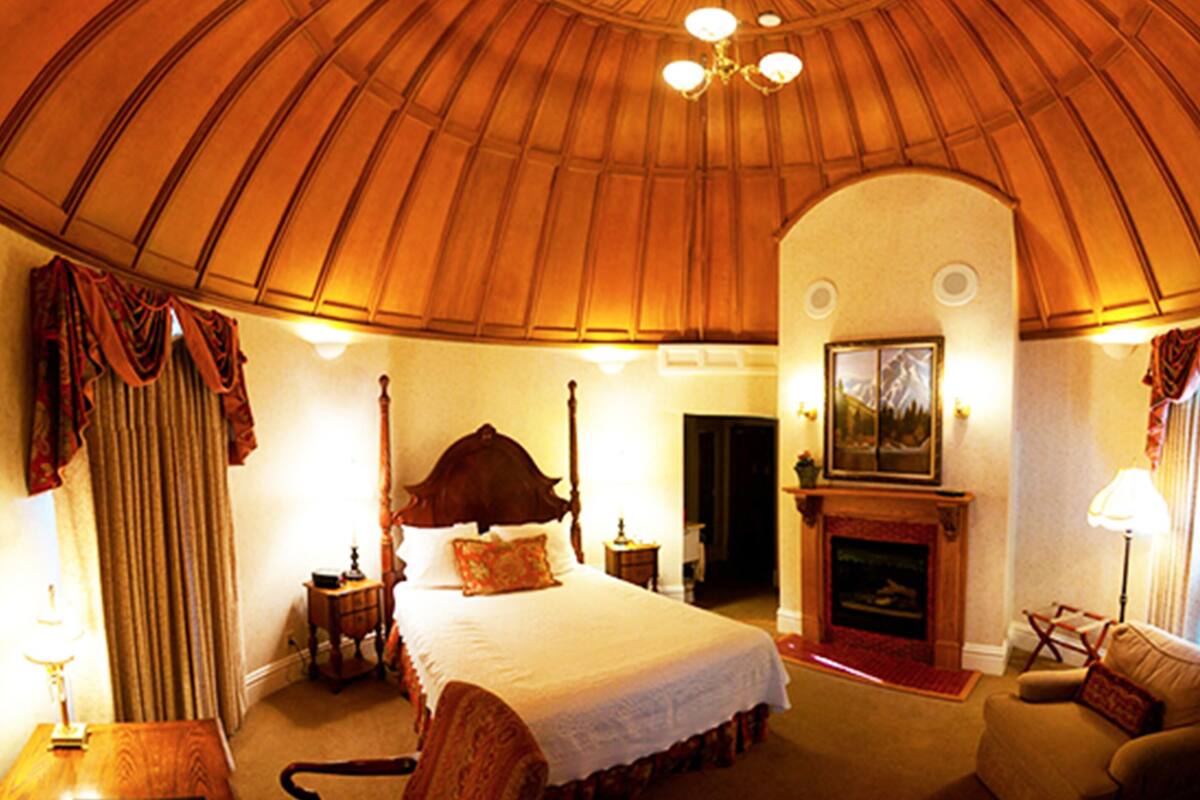 A room with a large bed, a fireplace, and a curved wooden ceiling.
