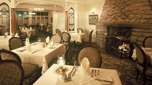 A dining area with tables set for service, a stone fireplace, and ornate architectural details. - Cliff House at Pikes Peak (Manitou Springs)
