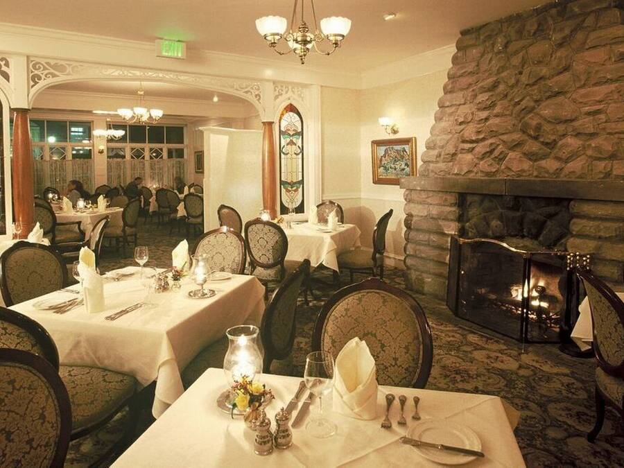 A dining area with tables set for service, a stone fireplace, and ornate architectural details.