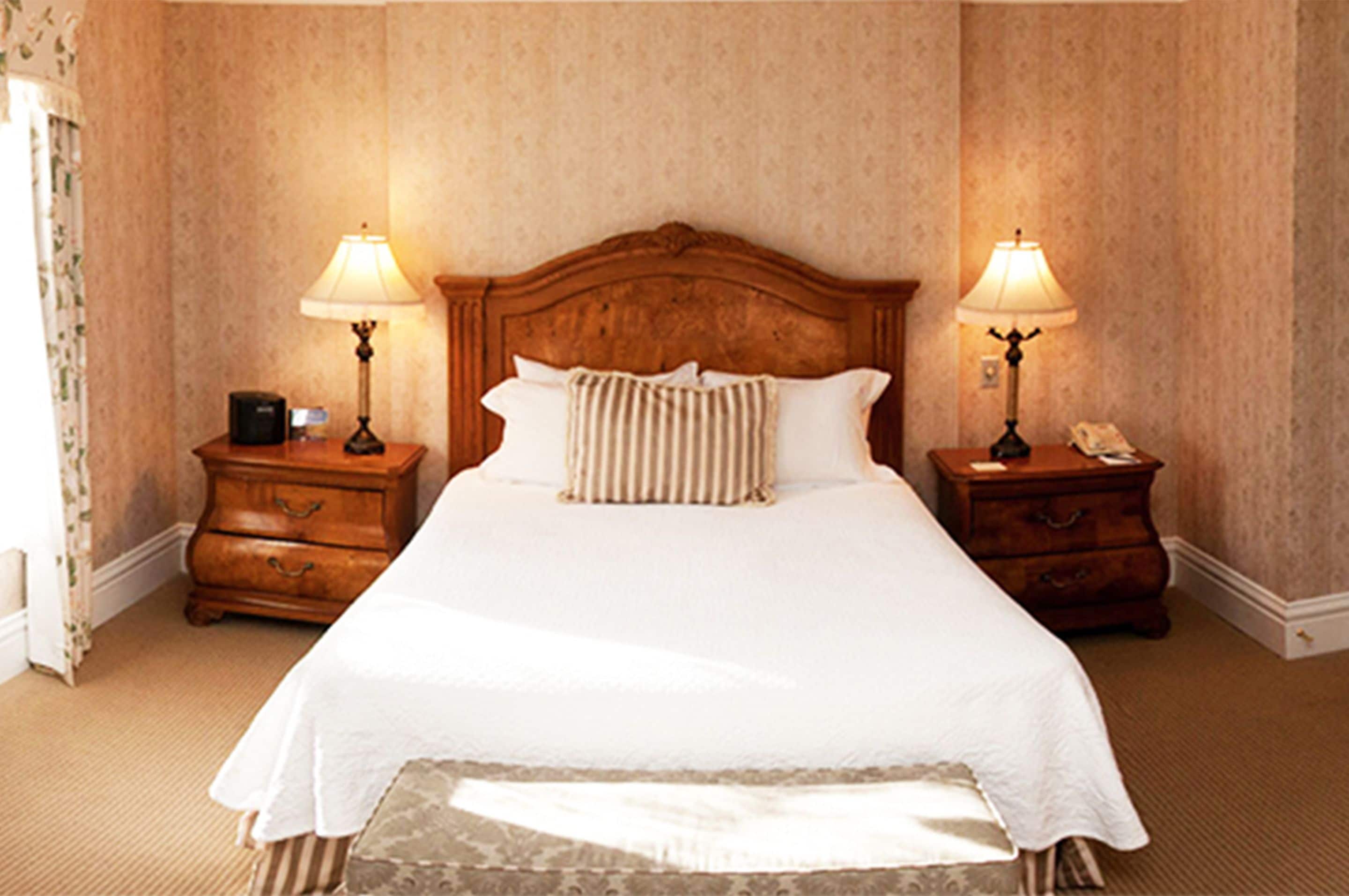 A neatly made bed with a wooden headboard, two bedside tables with lamps, and a striped pillow.