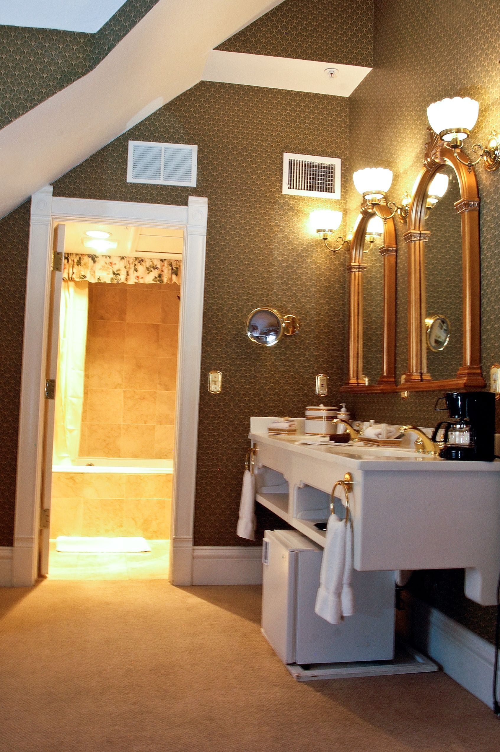A bathroom with a double sink, vanity, and a large mirror. There is a shower visible through an open door.