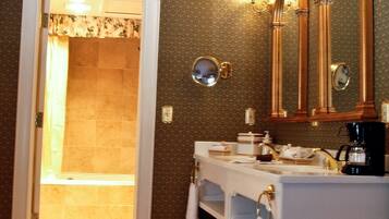 A bathroom with a double sink, vanity, and a large mirror. There is a shower visible through an open door.
