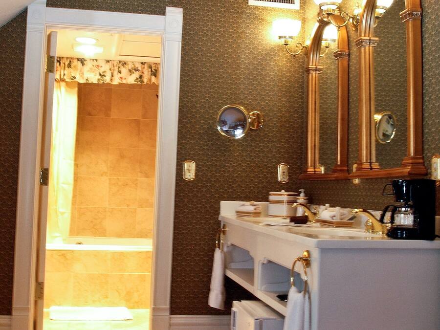 A bathroom with a double sink, vanity, and a large mirror. There is a shower visible through an open door.