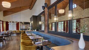 Een ruim restaurant met hoge plafonds, houten balken en grote ramen met uitzicht op de omgeving.